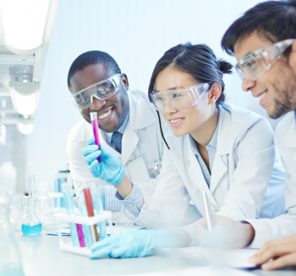 three scientists wearing lab coats and goggles looking at test tubes